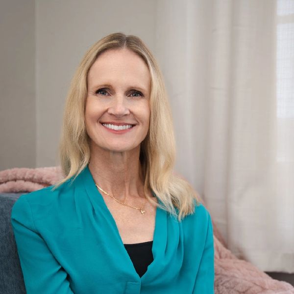 Smiling woman in teal blouse sitting on a blue chair indoors.