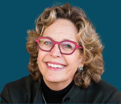 Smiling woman with curly hair and pink glasses.