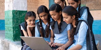 Group of schoolgirls using a laptop together, focused and engaged.