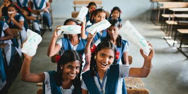 School girls happily holding sanitary pads in a classroom.