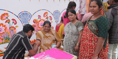 Women in traditional attire interacting at a colorful event.