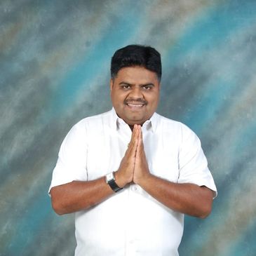 Man in white shirt with hands joined in greeting gesture.