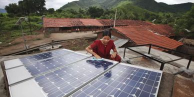 A woman cleans solar panels on a rooftop in a rural mountainous area.
