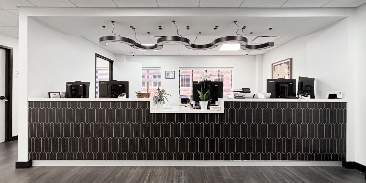 Modern office reception desk with black tile front and wave-shaped ceiling light.