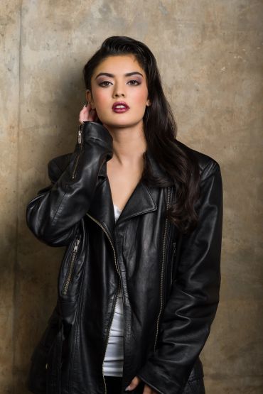 Confident woman in a black leather jacket poses against a textured wall.