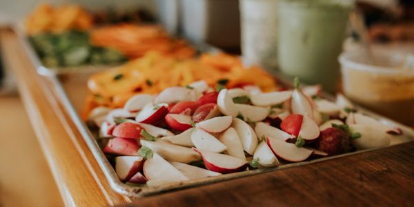 Tray of fresh sliced radishes with other vegetables in the background.
