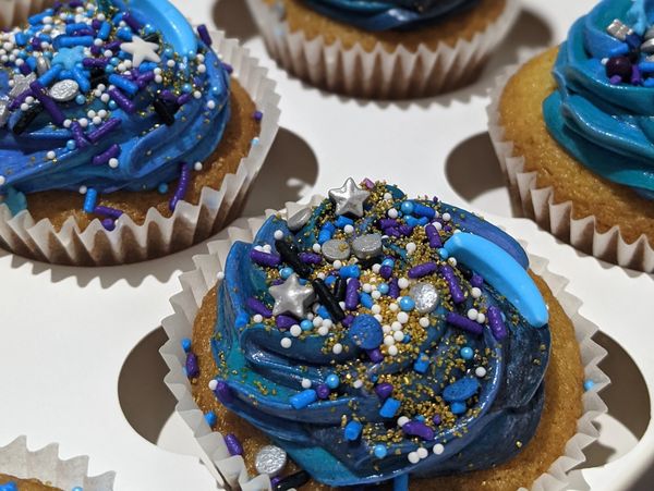 Cupcakes with galaxy-themed blue and purple frosting and star-shaped sprinkles.