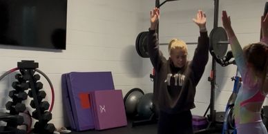 Two people exercising with arms raised in a home gym.