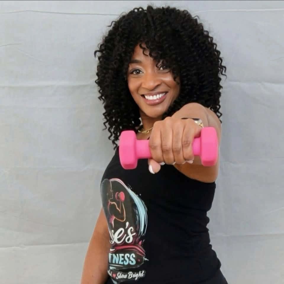 Smiling woman holding a pink dumbbell towards the camera.