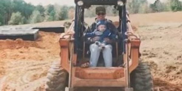 Adult and child riding a bulldozer on a dirt site.