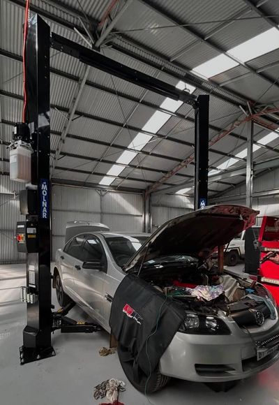 Silver car in garage with hood open for repair.