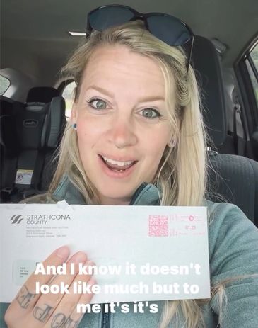 Krystal Jones smiling inside a car holding an envelope from Strathcona County.  Another happily received art awards to recognize her hard work for glass art