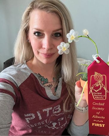 Krystal Jones holding a first-place ribbon from Orchid Society of Alberta with her glass orchid