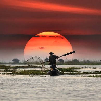 Fisherman rowing boat during large sunset.