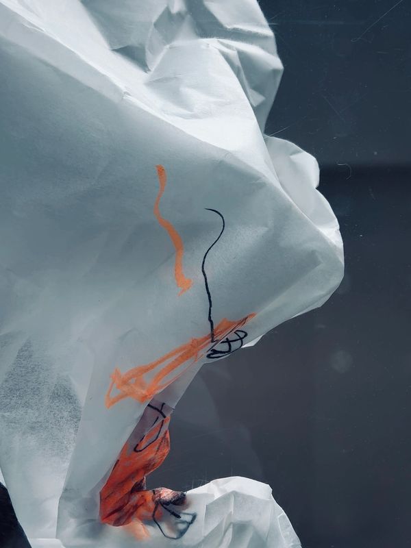 Close-up of crumpled white paper with orange and black scribbles.