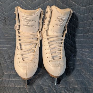 Pair of white figure ice skates with laces, placed side by side on a quilted surface.