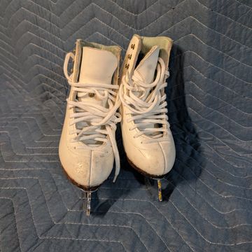 A pair of white figure skates with laces on a padded surface.