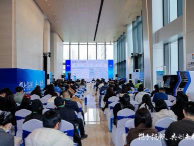 Audience attending a conference or seminar in a large hall with presentation screens.