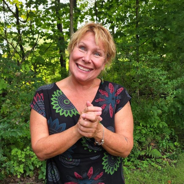 Femme souriante en tenue colorée devant un fond de verdure.