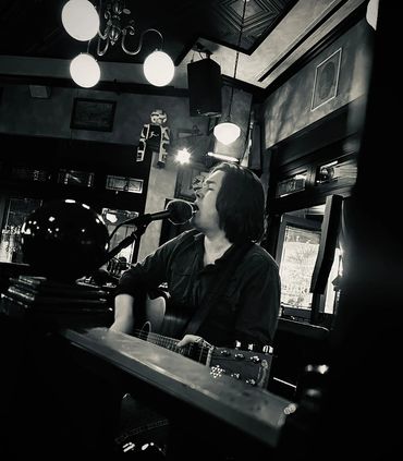 Black and white photo of a musician passionately singing and playing guitar indoors.