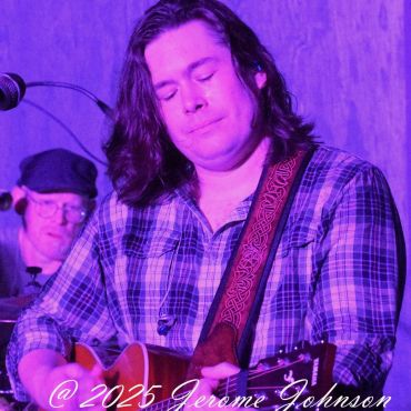 Musician passionately playing guitar under purple stage lights.