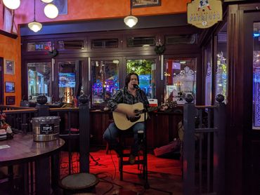 A musician plays guitar in a cozy, warmly lit pub.