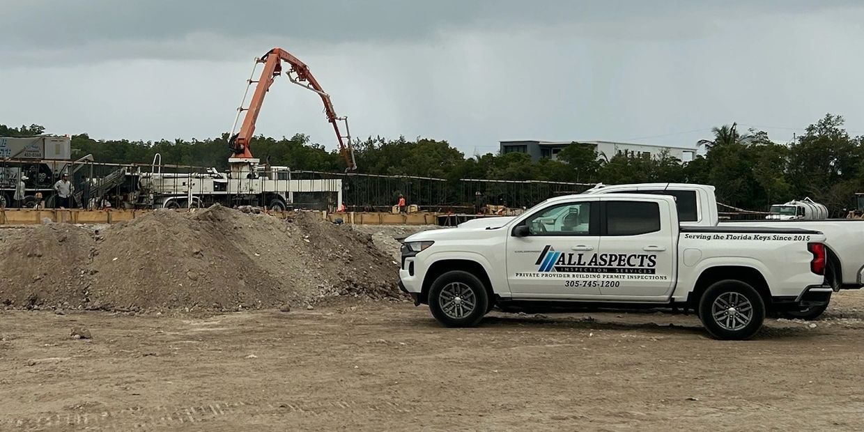 White truck from All Aspects Inspection Services at a construction site with equipment in the background.
