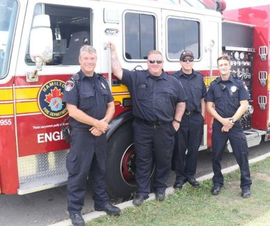 Four firefighters posing by a fire truck.