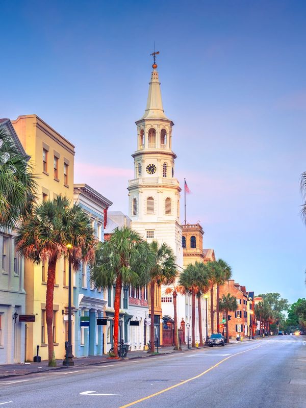 Historic street with palm trees and clock tower at sunset.