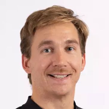Smiling man with light brown hair and a mustache against a white background.