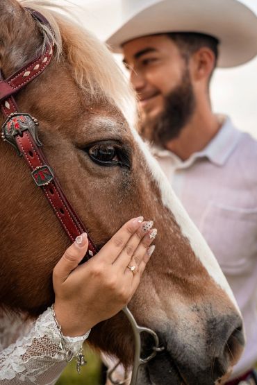 Woman's hand touching a horse's face with a man smiling in the background.
