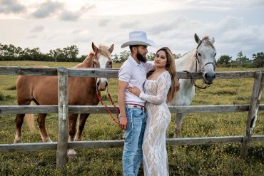 Couple posing with two horses by a wooden fence.
