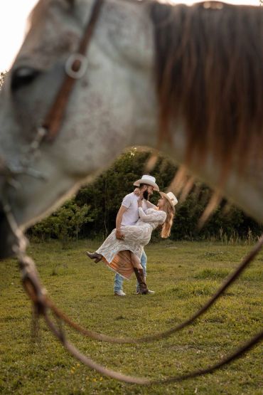 Couple in cowboy hats embraced through horse reins.