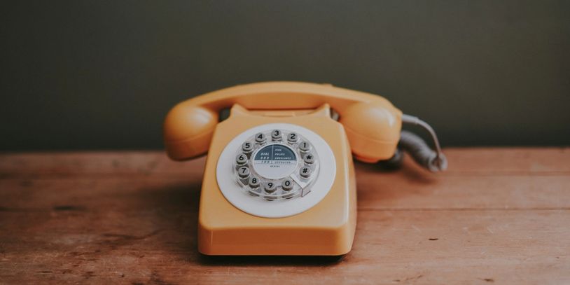 Vintage yellow rotary dial telephone on a wooden surface.