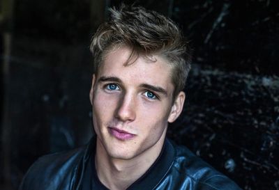 Portrait of a young man with blue eyes and tousled hair in a dark jacket.
