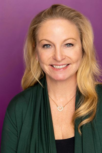 Smiling blonde woman with blue eyes against a purple background.
