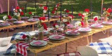 Outdoor picnic setup with low tables, cushions, and floral decorations under umbrellas.