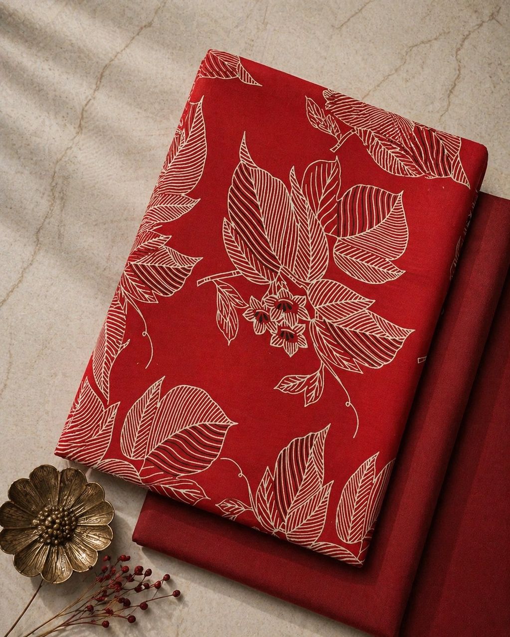 Red fabric with white leaf patterns neatly folded on a marble surface.