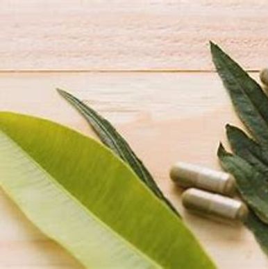 Herbal leaves with natural supplement capsules on a wooden surface.