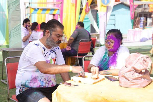 Couple with colorful Holi powder on faces enjoying food outdoors.