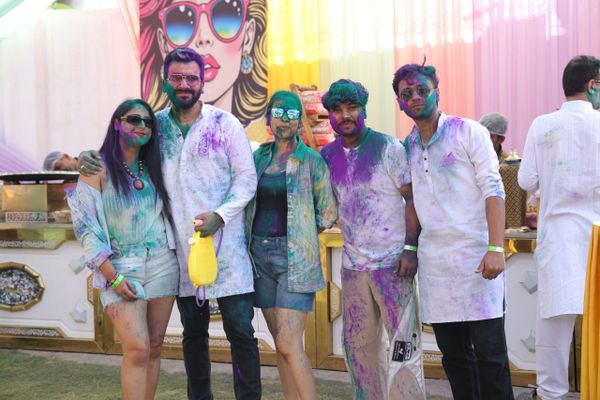 Group of friends covered in colorful powder celebrating Holi outdoors.