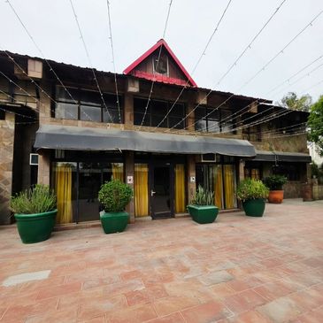 Front view of a rustic two-story building with large green potted plants.