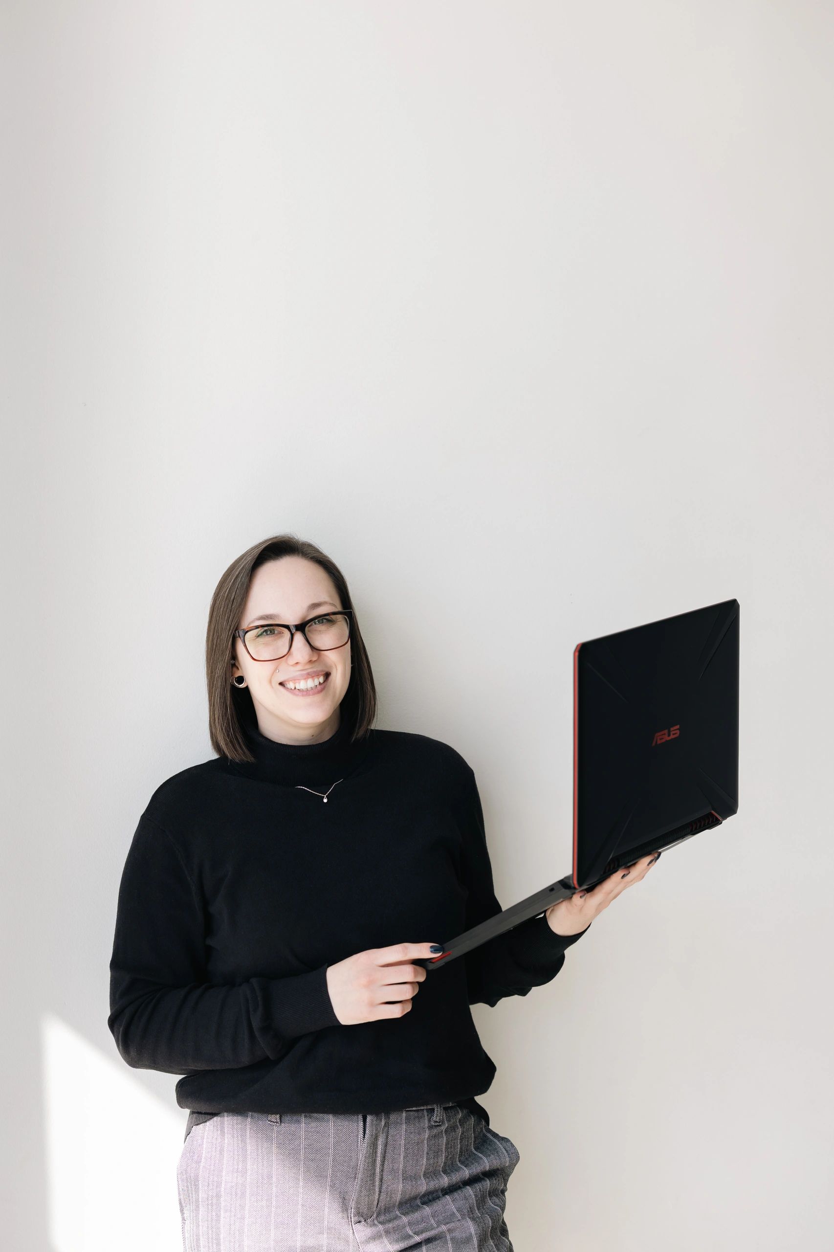 Smiling woman holding an ASUS laptop against a plain background.