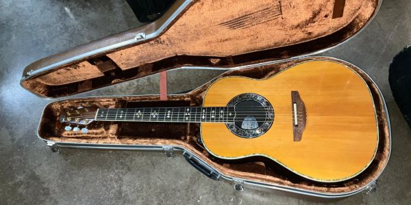 Acoustic guitar resting in an open hard case on a concrete floor.