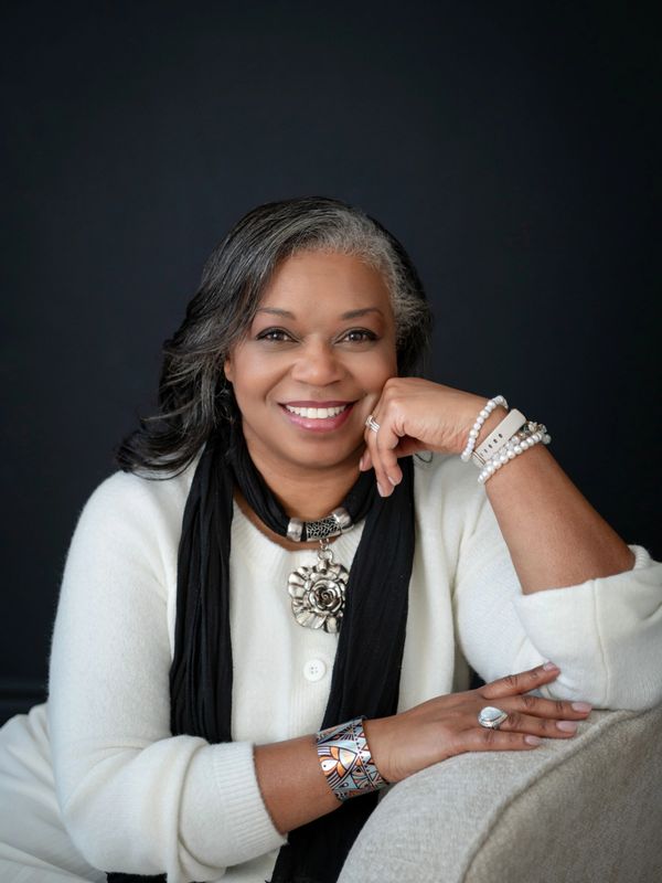 Smiling woman with silver-streaked hair wearing white and black, accessorized with jewelry.