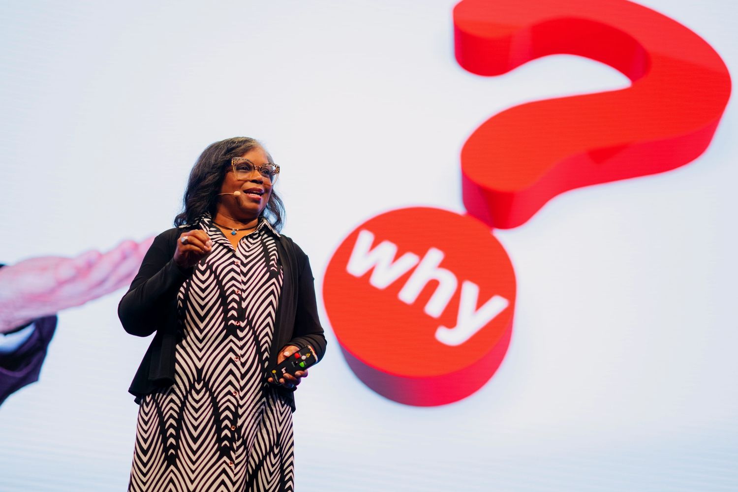 Julie Christiansen on stage speaking. Large graphic behind her asks, WHY?