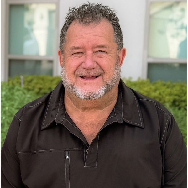 Smiling man with beard wearing black shirt outdoors.