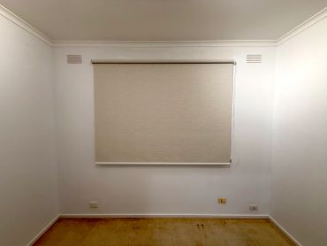 Empty room with beige walls and a window covered with a beige roller blind.
