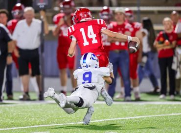 Football player in blue tackles a player in red during a game.