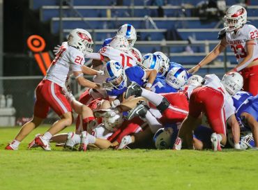 High school football players from two teams battling on the field during a game.